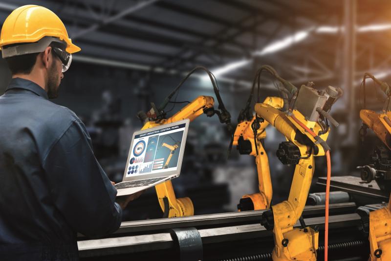 man controlling a robot using a laptop in an industrial environment