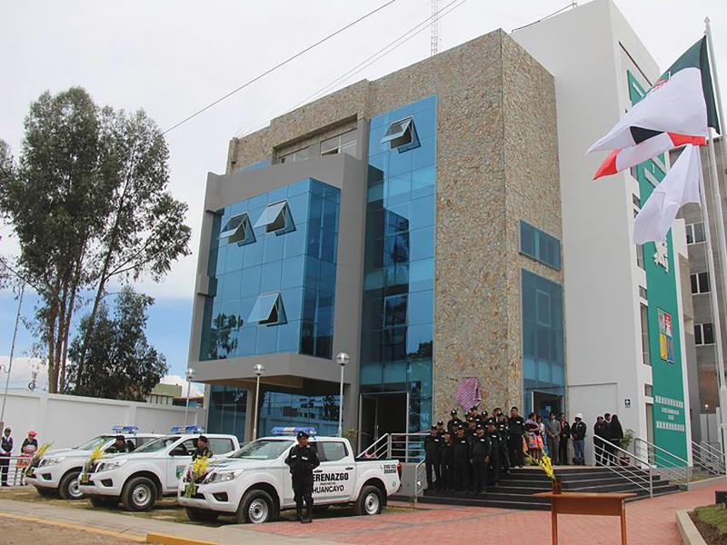 Municipality building with people, cars and flags in front.