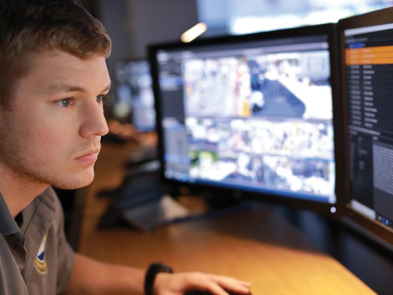 Man viewed from his right side, looking at monitoring computer screens.