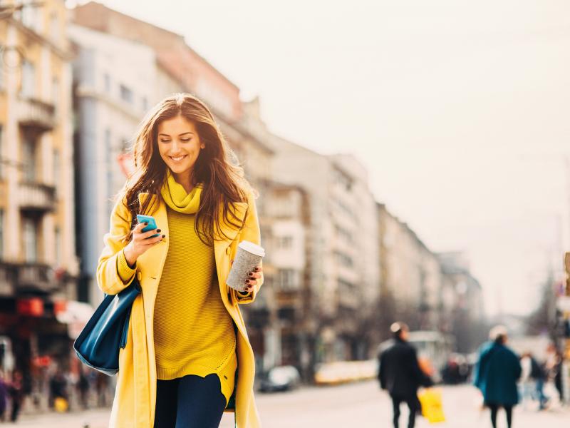 woman in yellow clothes, walks on a city street with her phone in her hand