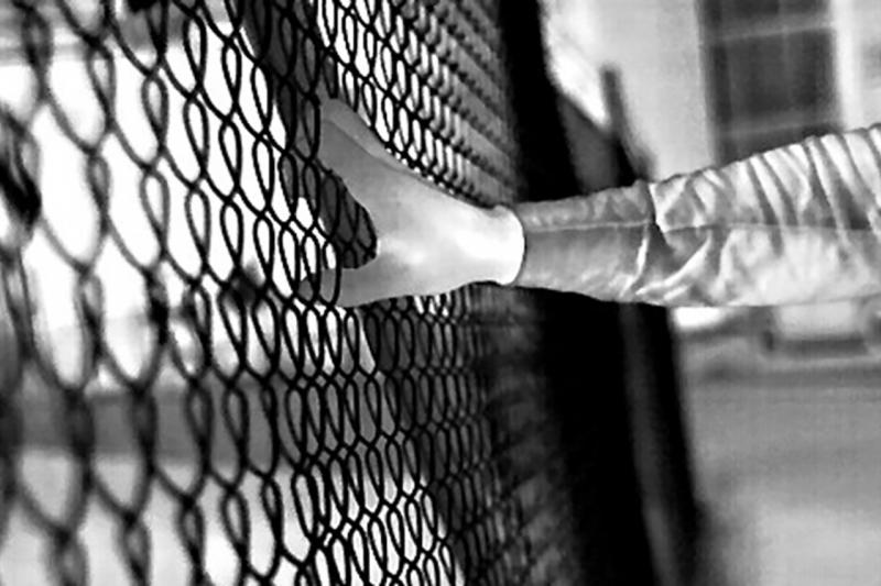Black and white footage of hand grabbing fence in the dark. 