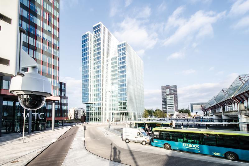 Axis Q60 with city in background, glass skyscraper and blue bus.