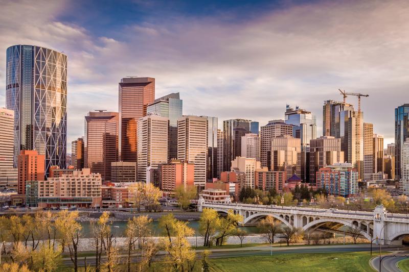 Skyline at sunset, skyscrapers in golden light, bridge and river in front.