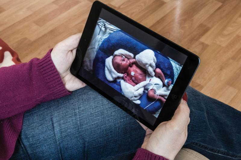 Female holding a tablet monitoring a newborn baby with tubes on body.