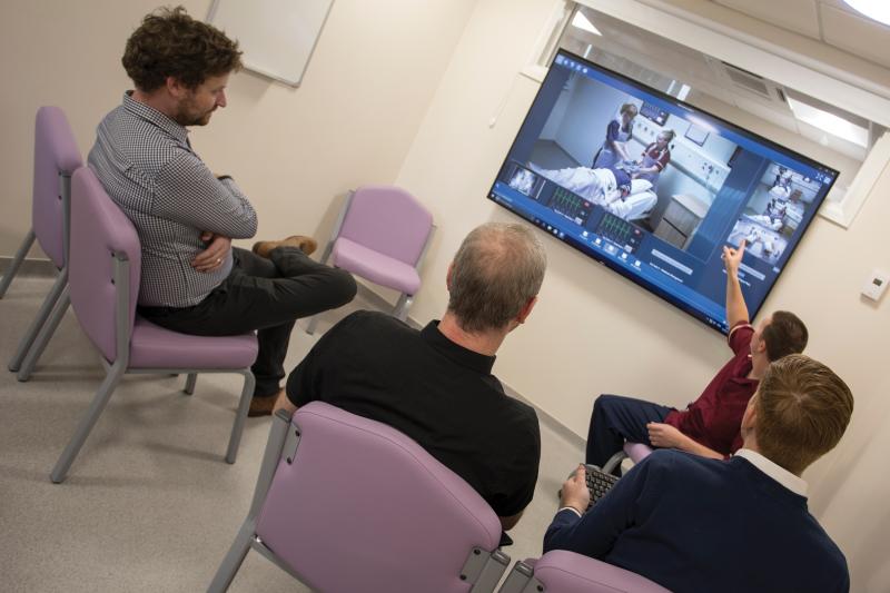 Three men and an instructor viewing a monitor screen of clinical training.