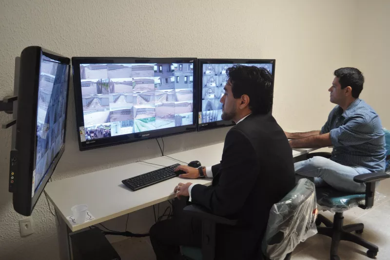 Two men monitoring prison through three screens. 