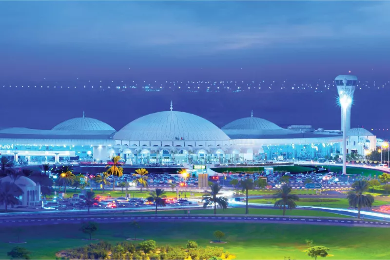 Exterior of airport in evening, white building and palm trees in front.