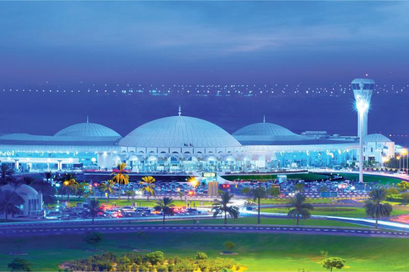 Exterior of airport in evening, white building and palm trees in front.