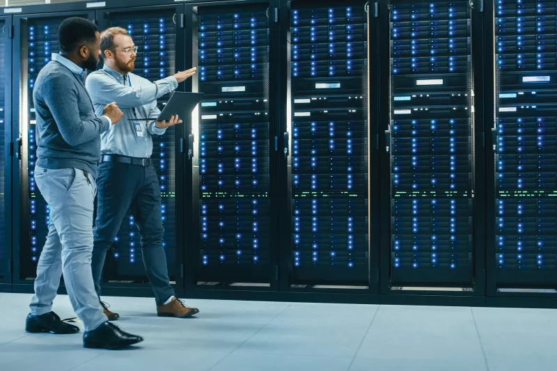 2 men walking along server racks and talking