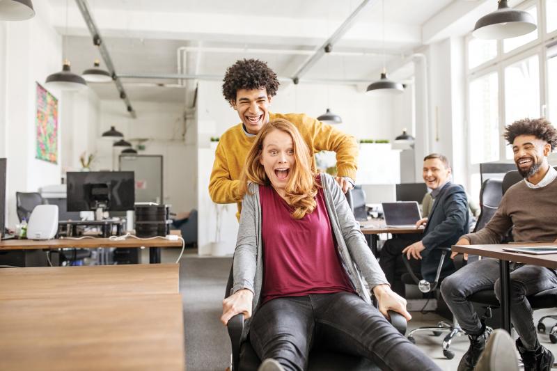 People playing inside office, pushing eachother on chairs.