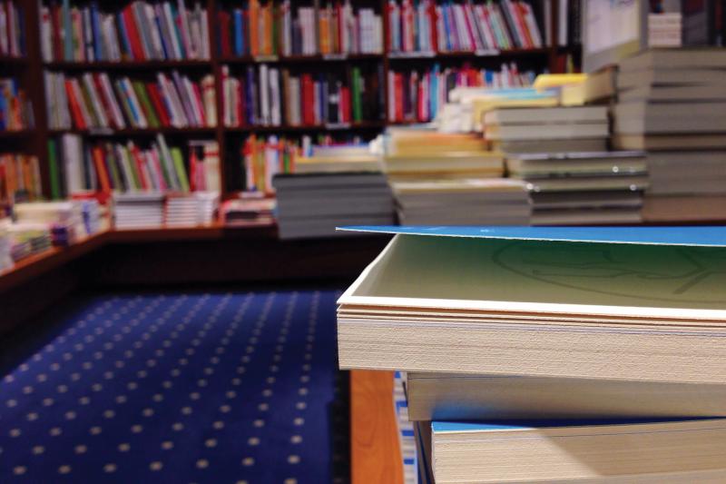 Stacked books with bookshelves in background