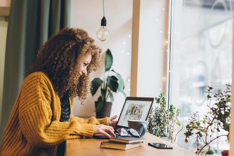 woman in yellow sweater works at her laptop