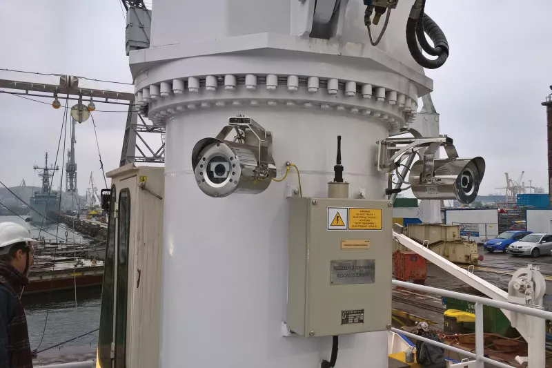 Cameras mounted on white pole on ship overlooking harbour. 