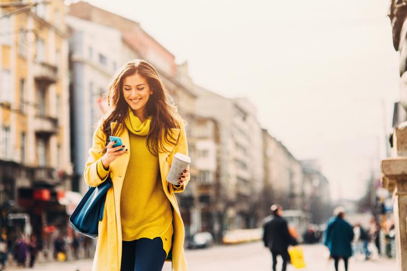 woman in yellow clothes, walks on a city street with her phone in her hand