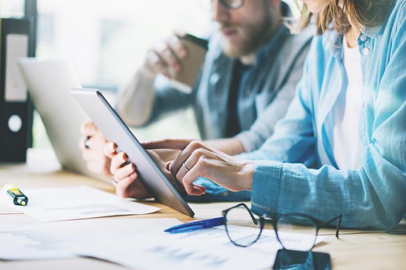 Two people sitting by a table looking at a notebook and tablet