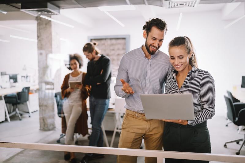 Man and woman are standing and looking at a laptop