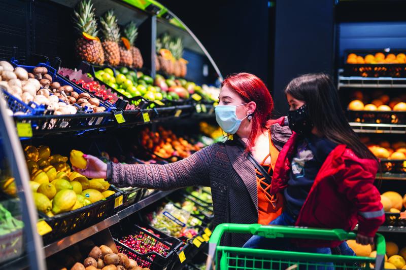 woman with child wearing face masks while shopping for fruit