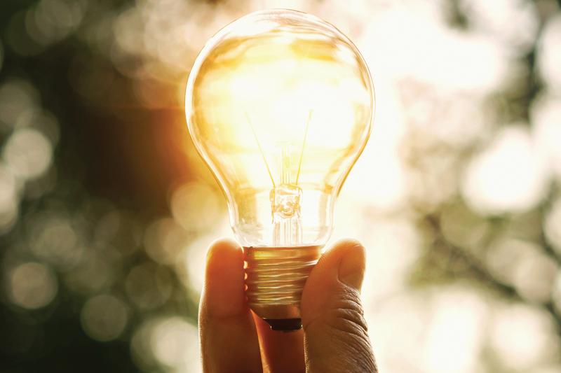 Hand holding lightbulb with outdoors backlight 