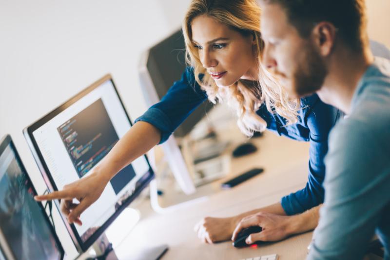 Two people in front of a computer screen, one of them pointing at it.