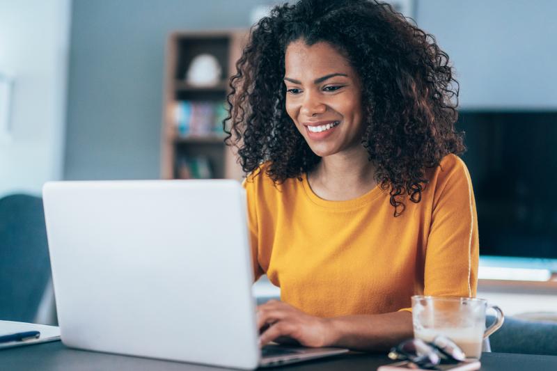 Smiling person with an orange shirt working on a laptop.