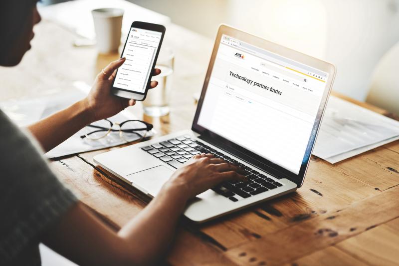 Person sittning by computer screen and holding phone