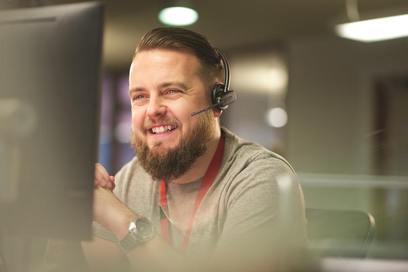man who is  sitting in front of a computer screen, wearing a headset, smiling