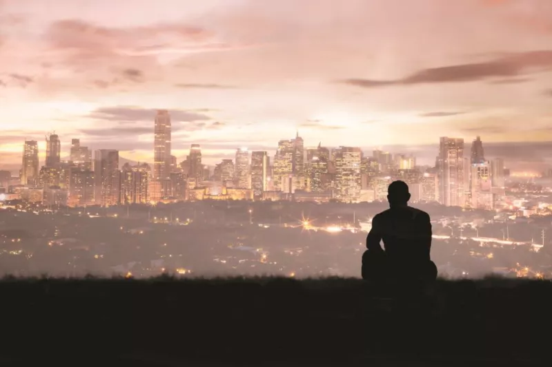 man_silhouette_sitting_overlooking_city