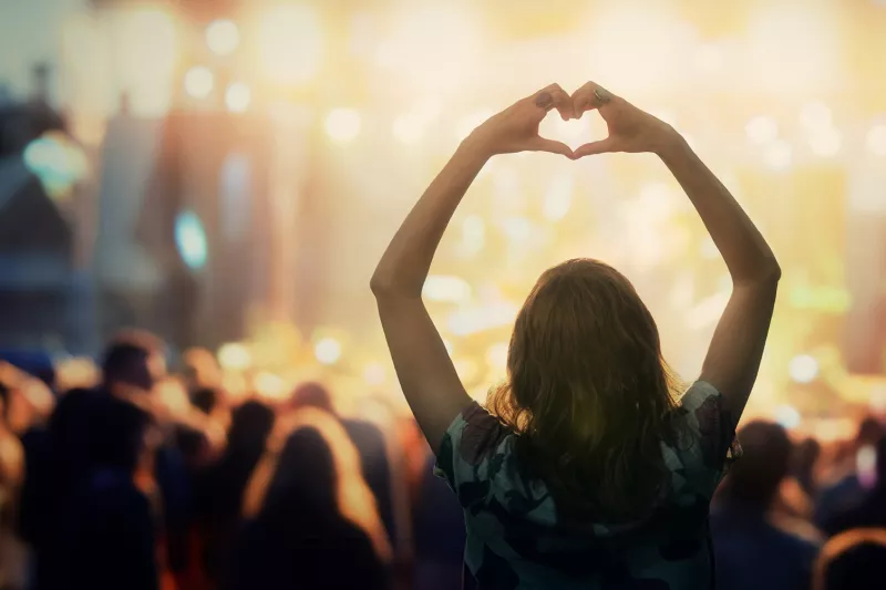 Concert with people and a woman holding hands shaped like a heart.
