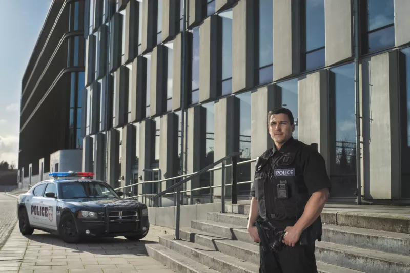 Police officer in black vest with police car