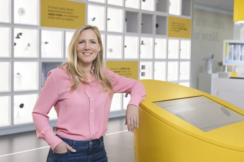 Anouska Östman is seen standing in Axis Experience Center smiling, while leaning against a yellow table.