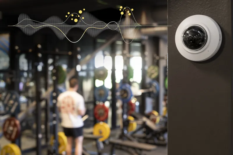 Camera with AXIS Audio Analytics mounted on a wall in a gym.