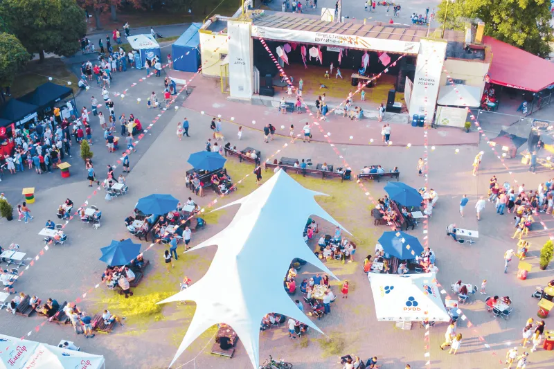 Aerial view of a summer concert in the park in the evening. There is a crowd under tents and around food stands.