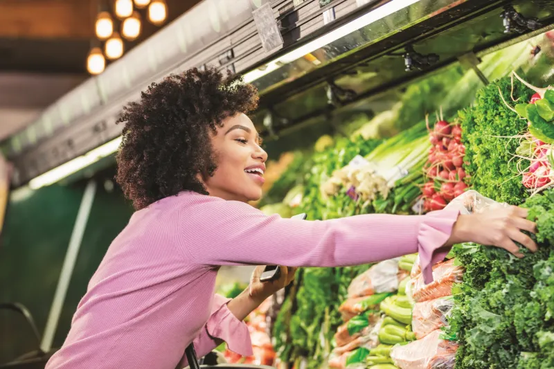 Woman happily reaching for a vegetable in a grocery store.