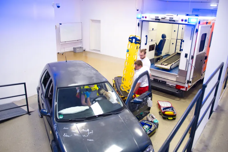 Paramedics practicing a vehicle rescue simulation with a car and ambulance in a training facility