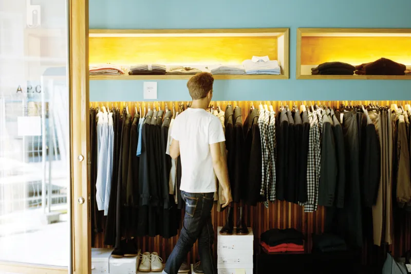 Man browsing in a clothing store with a shopping bag in his hand.