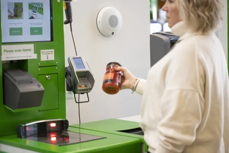A woman scanning an item in her hand at a grocery store self-checkout.