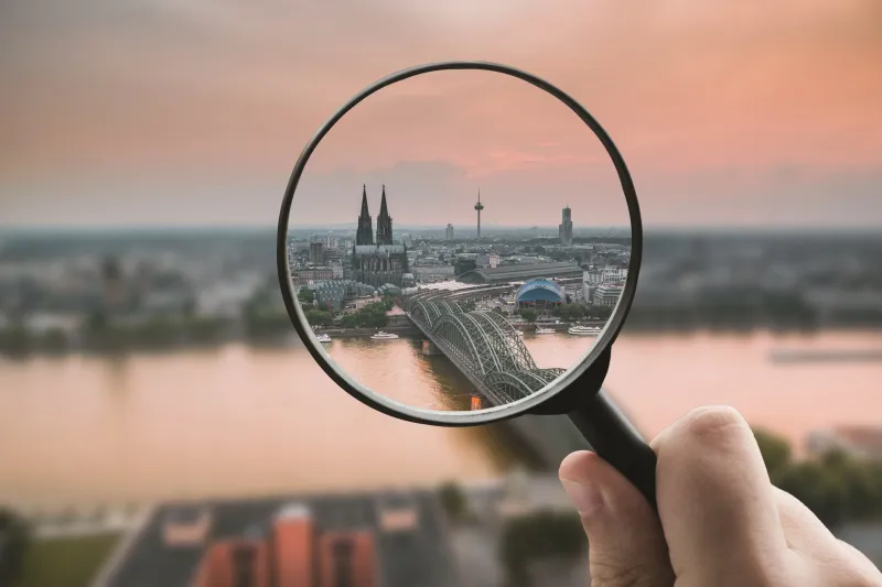 A city over the canal viewed from a magnifying glass during sunset. Everything outside the magnifying glass is blurred. 
