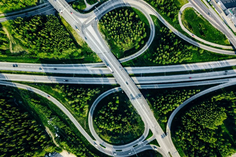 Overhead view of a highway overpass. The roads are surrounded by grass and trees.