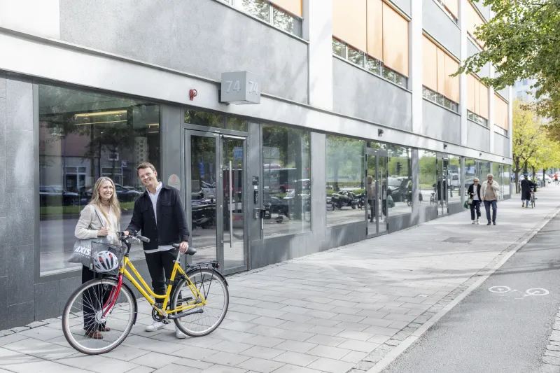 Two Axis colleagues standing outside the Stockholm office with an Axis-branded bicycle.