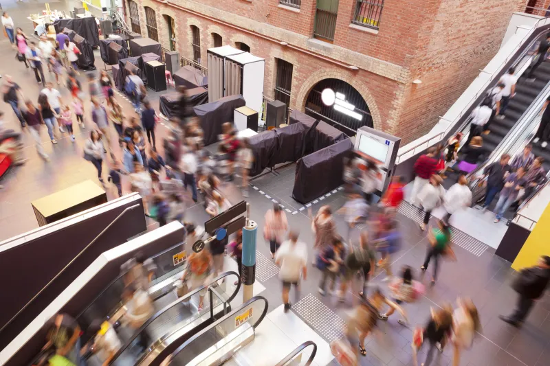 Aerial view inside a busy shopping mall. People are going up and down on the escalators.