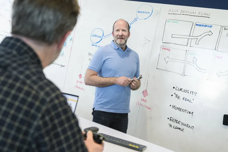 Thomas Ekdahl standing in front of a whiteboard, smiling and presenting his ideas to Axis colleagues.