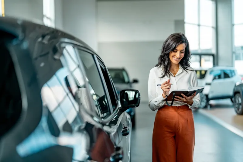 A saleswoman in a car dealership checking things off in a notebook.