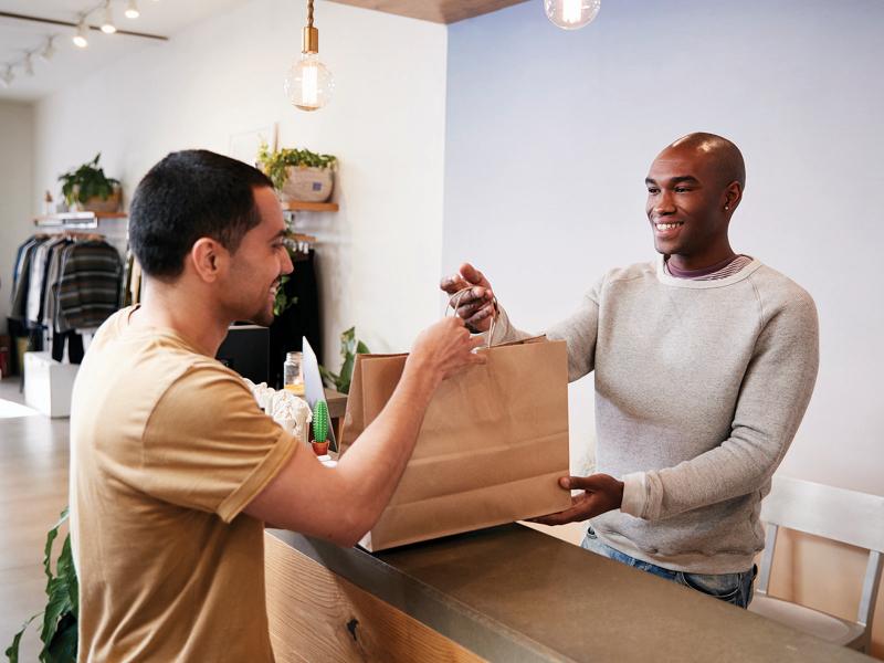 A man reaching for his shopping bag, over the counter in a retail store