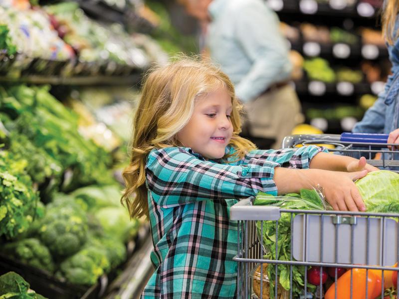 Child picking up vegetables in a grocery store