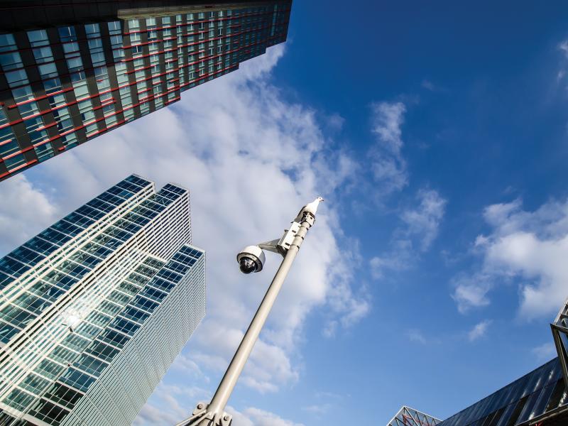 Axis Q60 on pole viewed from below, blue sky and skyscrapers around.