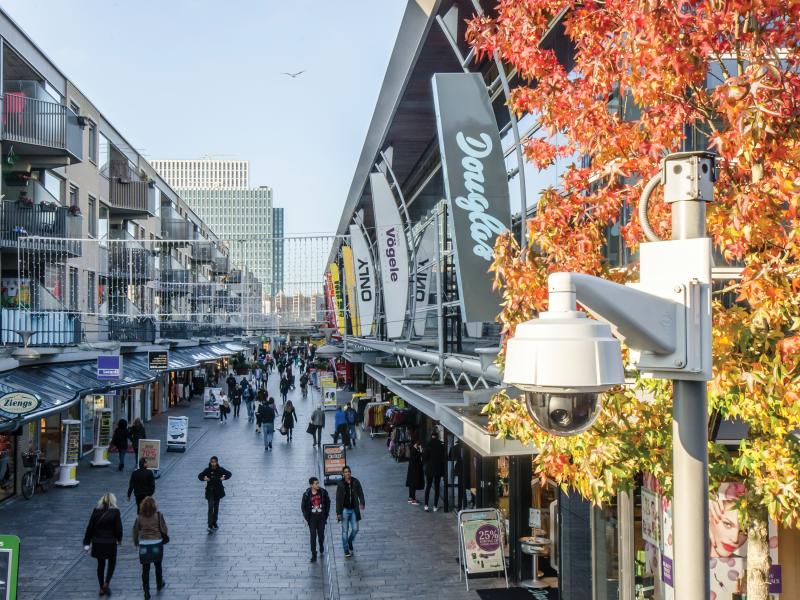 Axis Q60 on pole viewing street with people, signs and autumn tree.