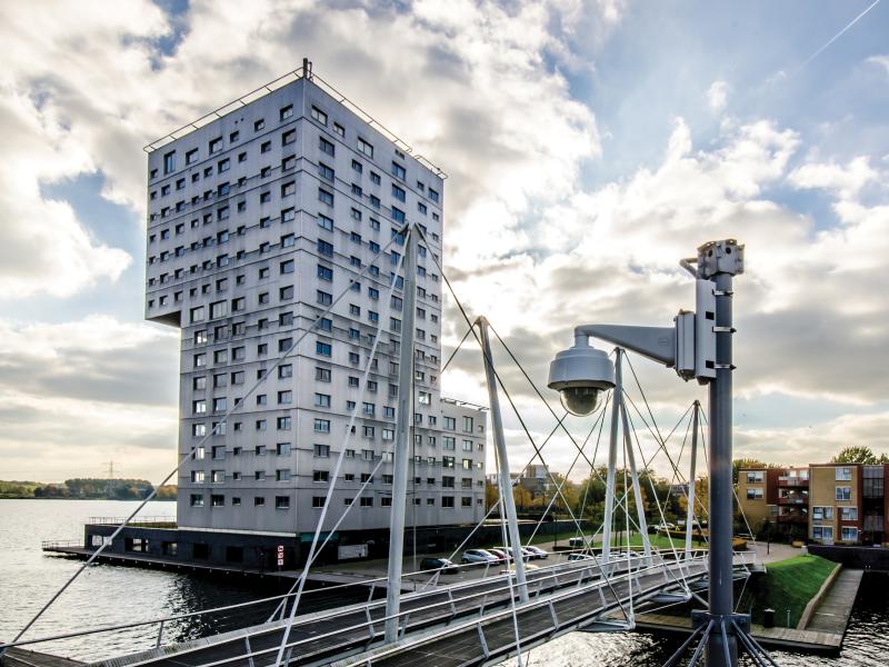 Axis pole camera by the waterfront, with bridge and one tall building.