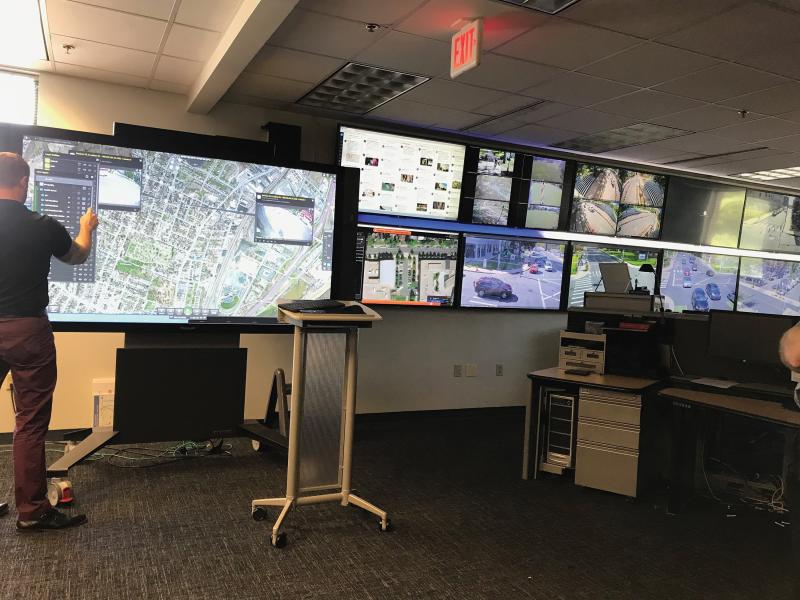 Man in big monitor room pointing at a big screen.