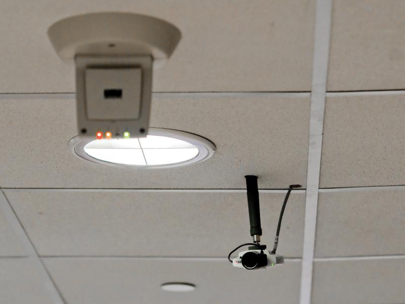 Axis camera on ceiling with a round window next to it.