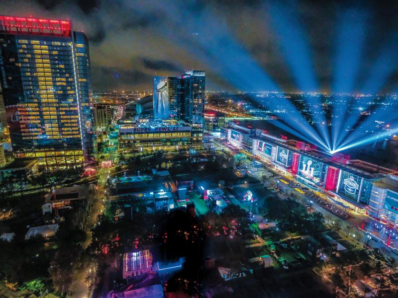 Superbowl city event area by night, blue light up in sky.